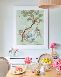 blue framed chinoiserie wall art print featuring antique inspired herons, flowers, and blossoms beneath a pine tree with butterflies hung on wall