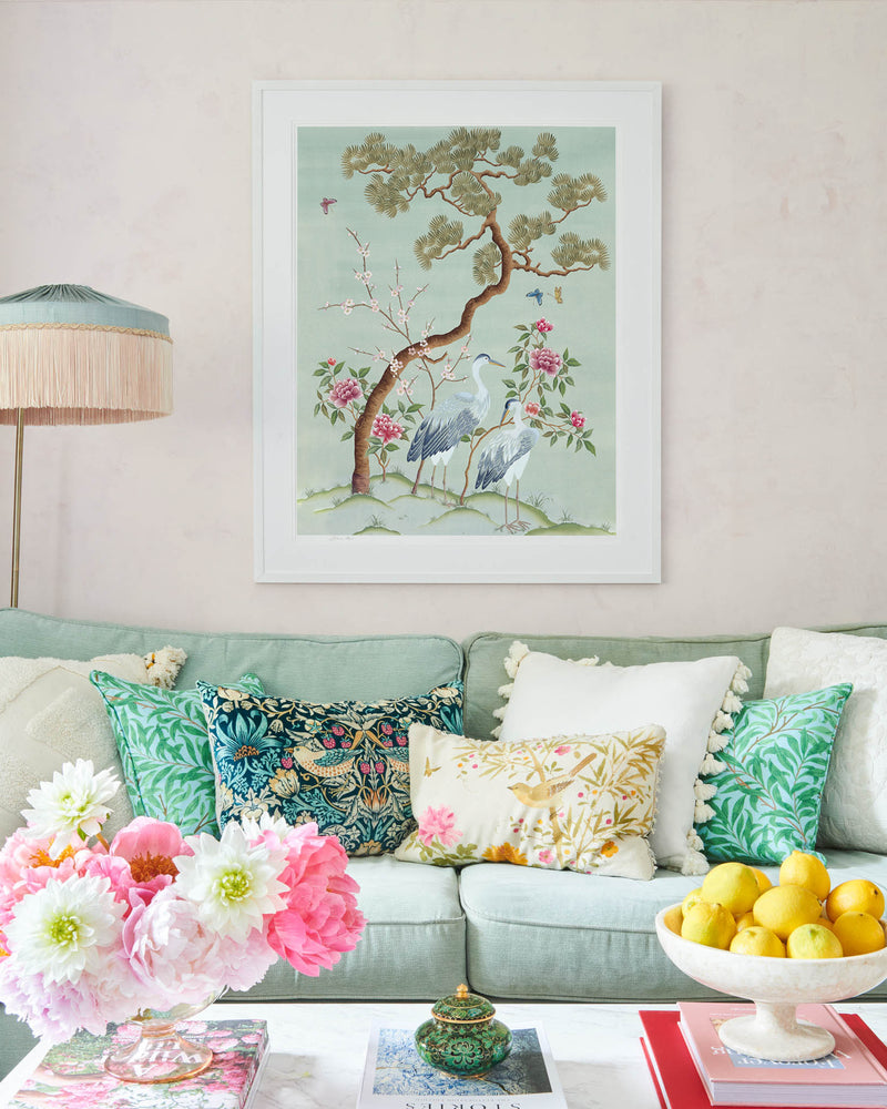 blue framed chinoiserie wall art print featuring antique inspired herons, flowers, and blossoms beneath a pine tree with butterflies hung on wall