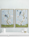 2 framed blue chinoiserie wall art prints with botanical illustrations featuring birds, butterflies, and flowers hung on wall