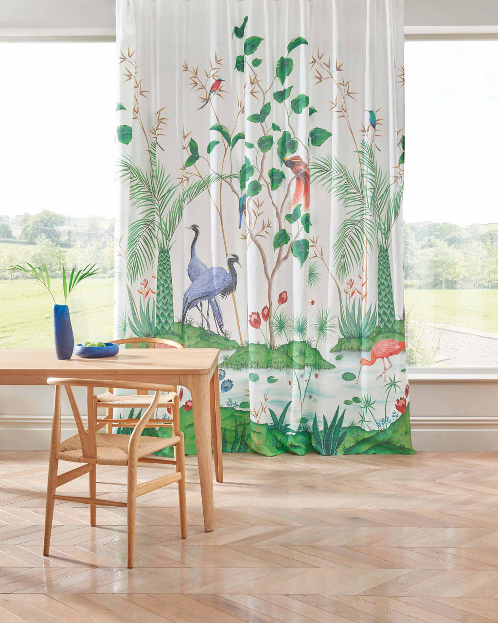 A stunning design created exclusively for Osborne & Little for their Empyrea range, featuring blue herons, palm trees and rambling botanicals. This image shows the fabric hanging as curtains