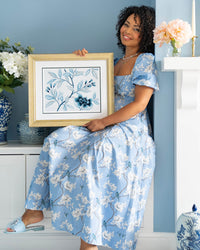 watercolour artist diane hill holding framed classic blue and white chinoiserie art print featuring flowers and branches with gold embellishment in regency style living room