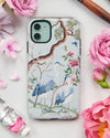 blue luxury chinoiserie phone case featuring antique inspired herons, flowers, and blossoms beneath a pine tree with butterflies