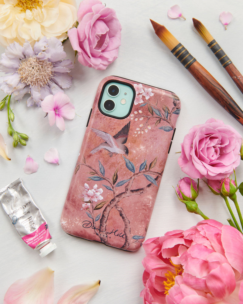 The Alexandra phone case by Diane Hill. Alexandra is a muted, vintage-inspired design featuring earthy tones and a distressed feel. A pretty little bird swoops above a branch laden with leaves and blossom. A styled flatlay set with peonies and paintbrushes