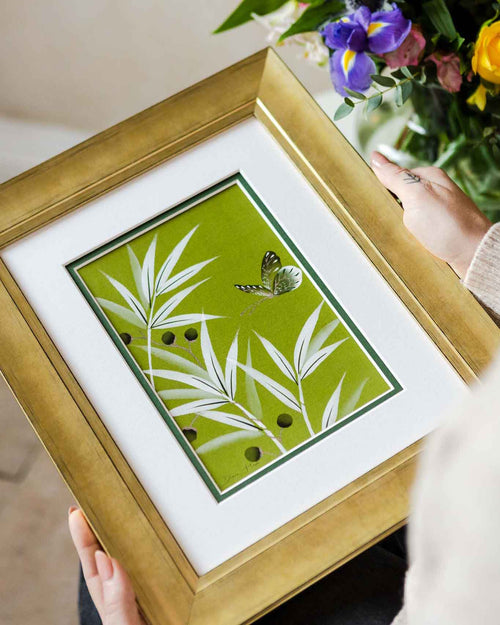hands holding framed green and white chinoiserie wall art print featuring bamboo a butterfly