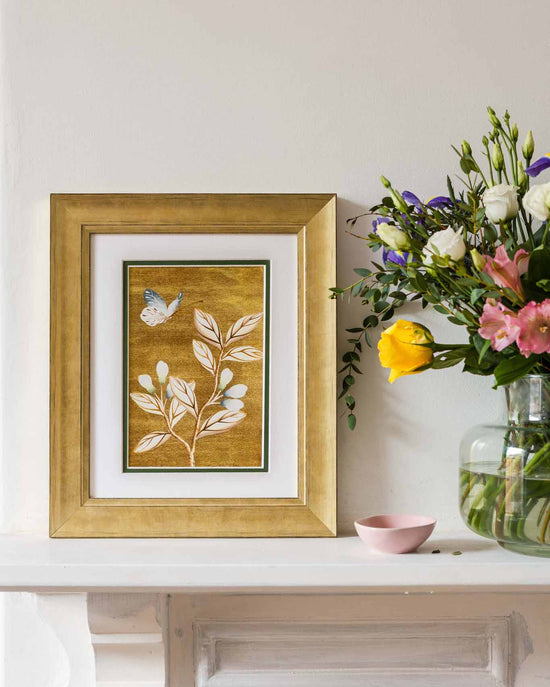 framed chinoiserie wall art print featuring vintage Chinese-style butterfly and flower branch on gold background on mantle