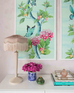A close up of an aqua blue Chinoiserie art print by Diane Hill featuring lush green  botanicals and pink hydrangea flowers. Framed in a white frame as a pair, above a living room console table