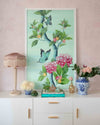 framed Chinoiserie style art print featuring butterflies and pink flowers on an aqua blue background hung on wall