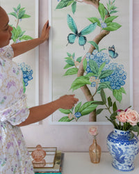 close up of pair of framed Chinoiserie style art prints featuring butterflies and blue flowers on an ivory cream background hung on wall