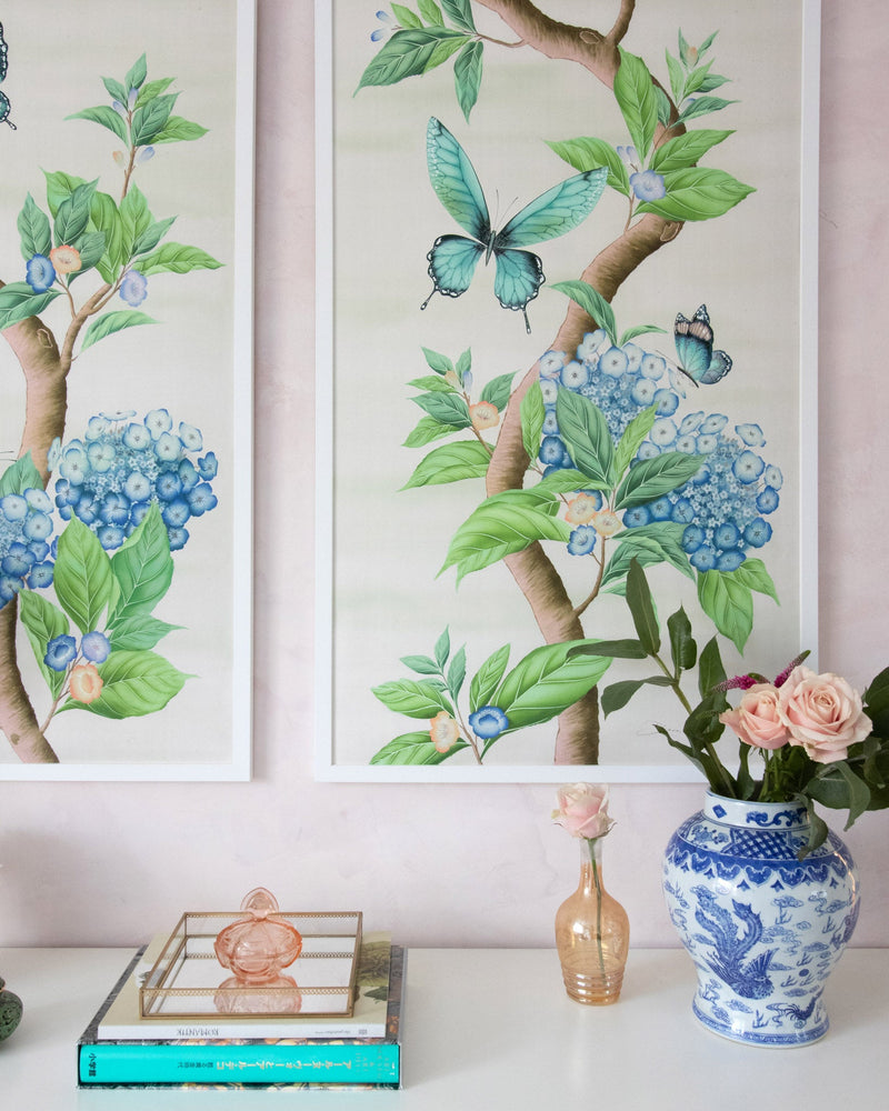 close up of pair of framed Chinoiserie style art prints featuring butterflies and blue flowers on an ivory cream background hung on wall