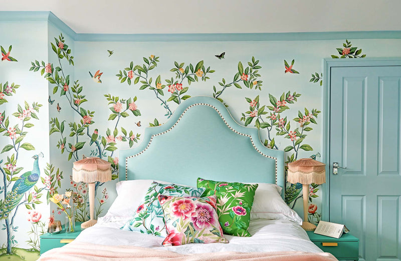 Florence chinoiserie wallpaper by diane hill and harlequin blue colourful with birds and butterflies big blue headboard two bedside tables and lamps and chinoiserie cushions on bed