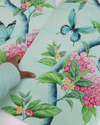 hand holding Chinoiserie style art prints featuring butterflies and pink flowers on an aqua blue background