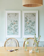 The Lilly and Mariya art print in pebble blue, framed side by side in a dining room in a classic white frame. A celebration of butterflies, bamboo and botanicals, Lilly is a beautiful modern chinoiserie art print which was originally hand-painted onto pure silk, featuring delicate leaves and an abundance of butterflies