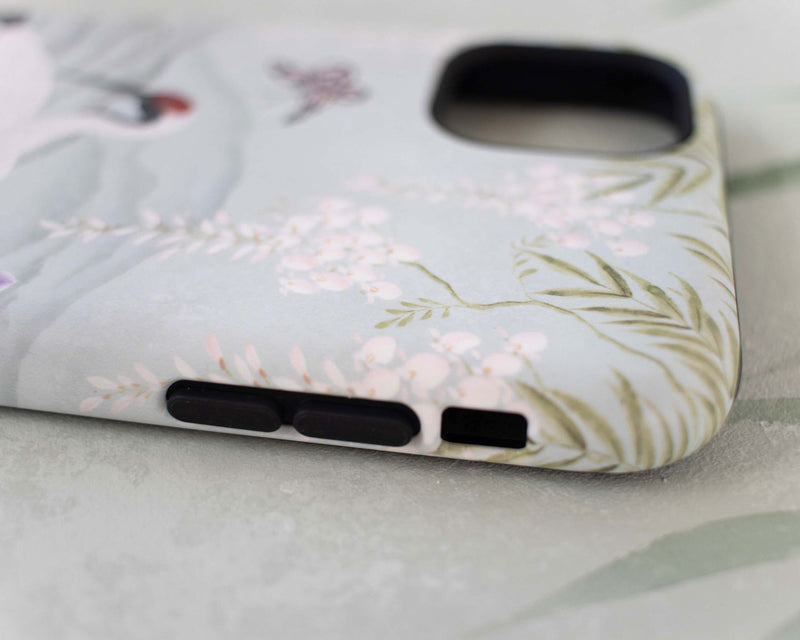 close up of luxury chinoiserie phone case featuring Japanese inspired crane, flowers, and wisteria on a blue mountain background