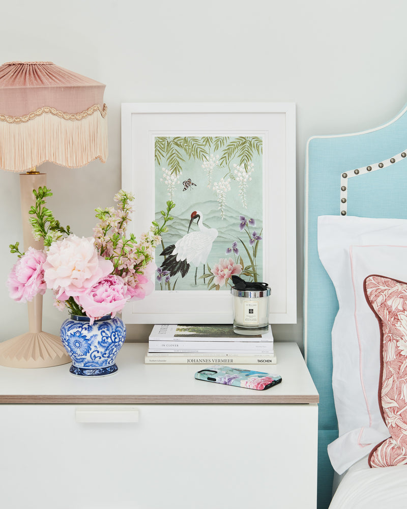 framed chinoiserie wall art print featuring Japanese inspired crane, flowers, and wisteria on a blue mountain background on bedside table