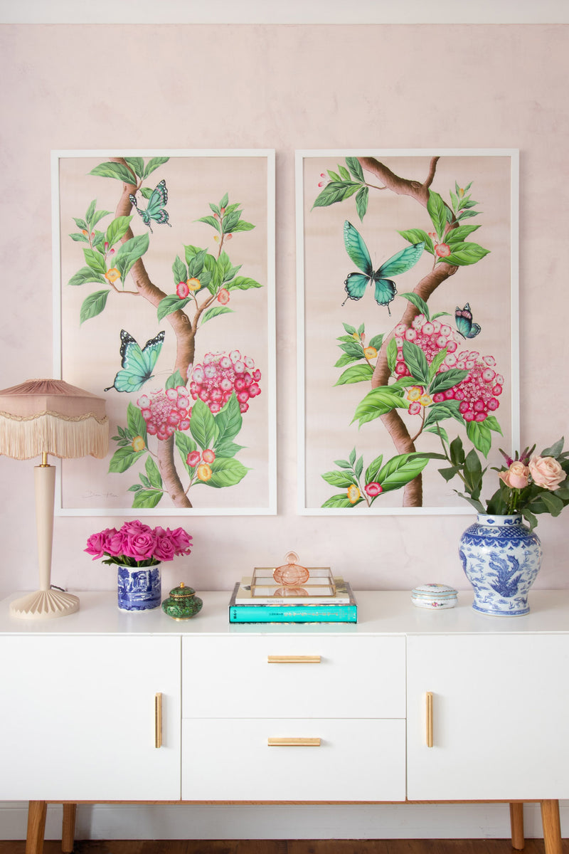 pair of framed Chinoiserie style art prints featuring butterflies and pink flowers on a pastel pink background hung on wall