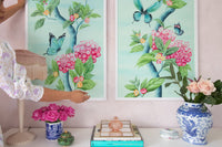 close up of a pair of two framed Chinoiserie style art prints featuring butterflies and pink flowers on an aqua blue background hung on wall