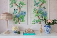 pair of two framed Chinoiserie style art prints featuring butterflies and blue flowers on an ivory cream background hung on wall