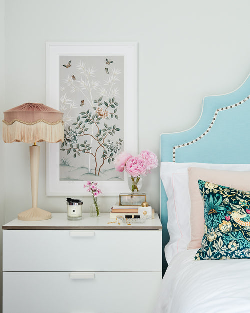 Lilly chinoiserie art print by Diane Hill features blue tones, peonies and butterflies. The print is framed above a bedside table set with flowers and candles