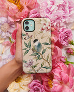 A hand holds the Rosie phone case by Diane Hill, with peonies in the background. Featuring a pretty songbird perched on a branch with butterflies overhead and an abundance of blooming peonies in the background.