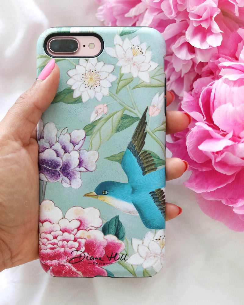 A hand holds the Shona phone case by Diane Hill, with an abundance of peonies in the background. Shona is a brilliantly colourful and elegant design with a subtle antique feel, featuring a joyful blue bird, water lilies, peonies and leaves.