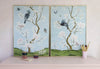 pair of 2 framed blue chinoiserie wall art prints with botanical illustrations featuring birds, butterflies, and flowers hung on wall