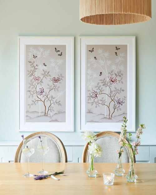 pair of two soft pink framed chinoiserie wall art prints featuring butterflies, flower branches, and bamboo hung on wall